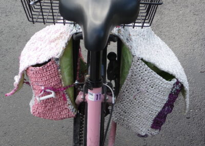 Poches à vélo rose, blanche et violette en plastique crocheté, dos en toile cirée et fixées avec une tresse en fil de plastique et bobines de fil. CHF 120.- sur commande uniquement